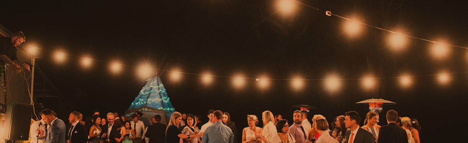 Brazilian BBQ catering event at night, guests enjoing themselevs with fairy lights strung above